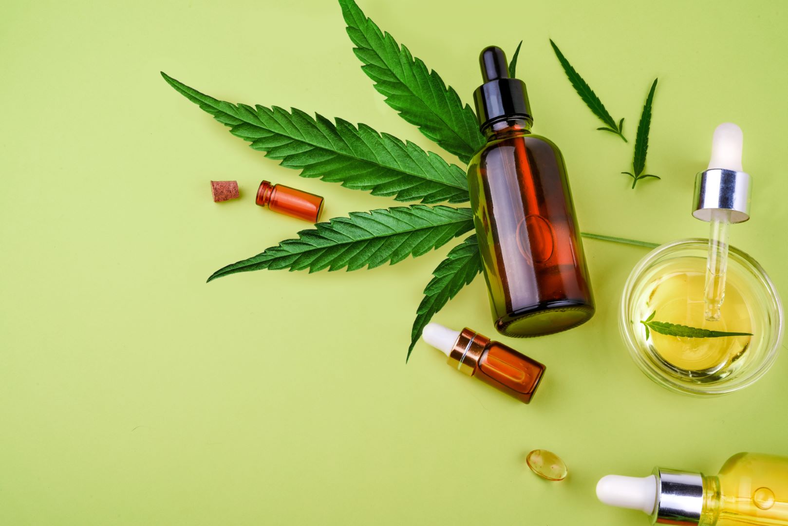 A photo of different glass bottles with CBD oil, a THC tincture and a cannabis leaf.