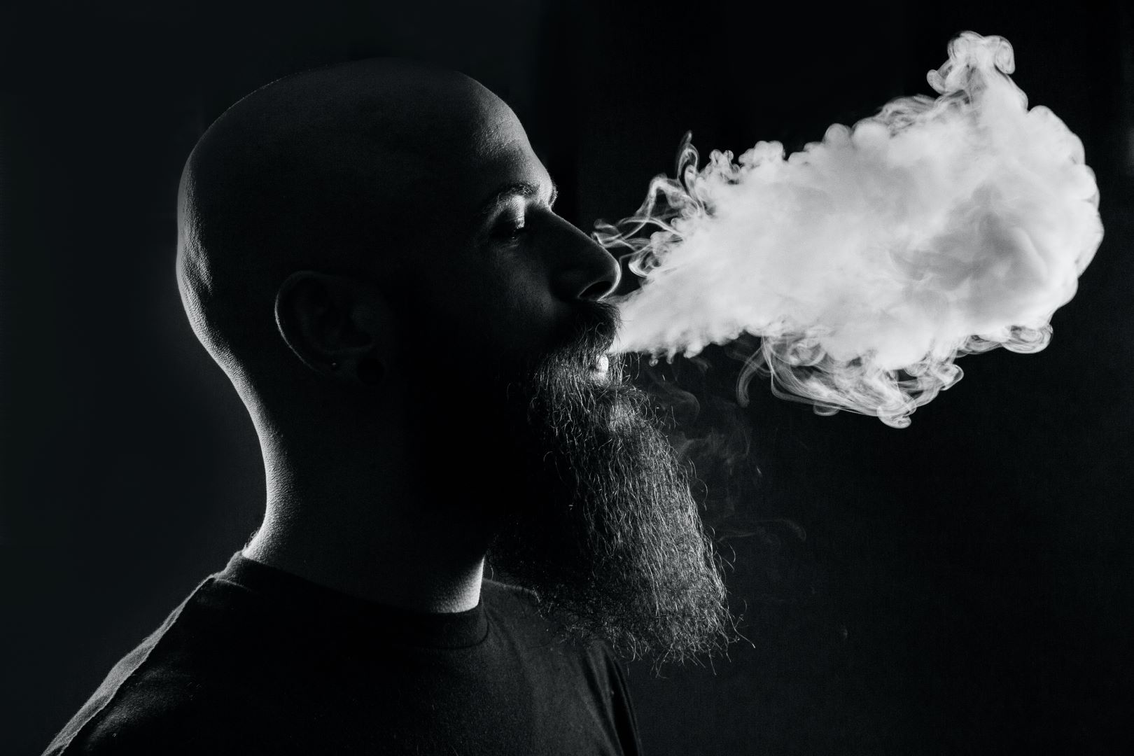 A photo of a bearded man smoking a vape pen
